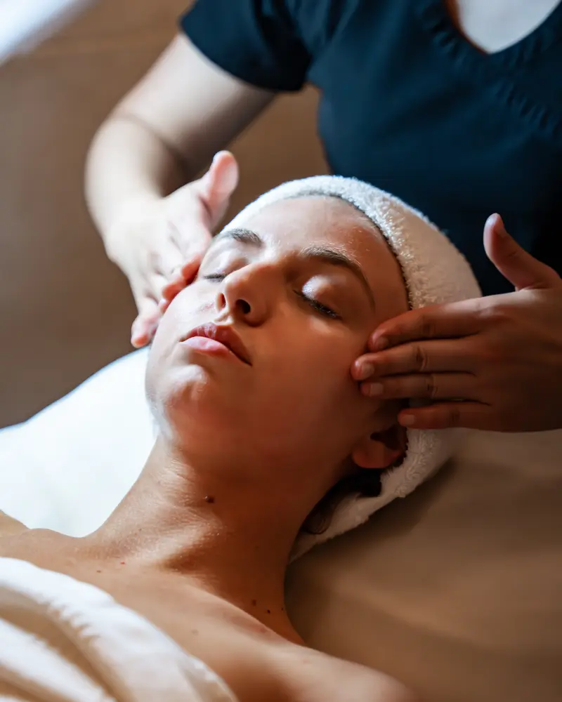 An esthetician's hands rest at a client's temples during a facial
